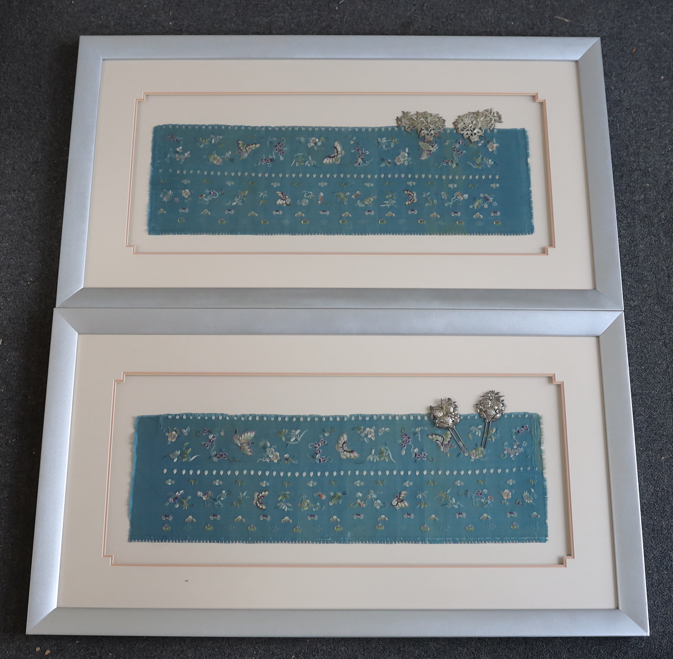 A pair of late 19th century Chinese blue silk multi-coloured embroidered panels, possibly a pair of wide sleeve bands to a robe, each mounted with two white metal ornaments, 19cm wide, 61cm high